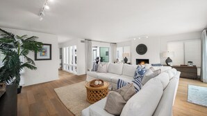 A modern living room with a white sofa, a fireplace, and a large plant. - Coastal Getaway in Corona Del Mar (Corona Del Mar)