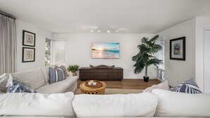 A modern living room with a sofa, a coffee table, and a TV. There are framed pictures on the walls and a plant in the corner. - Coastal Getaway in Corona Del Mar (Corona Del Mar)