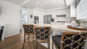 A modern kitchen with white cabinetry, a central island, and two bar stools. - Coastal Getaway in Corona Del Mar (Corona Del Mar)