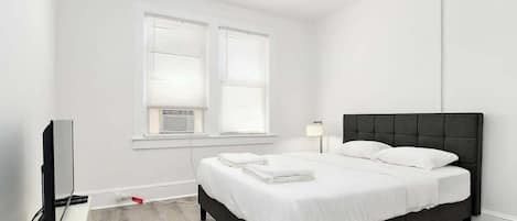 A bedroom with a bed, a TV, and a window with blinds.