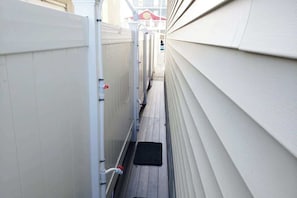 A narrow pathway between two buildings with a white fence and a black mat at the entrance.