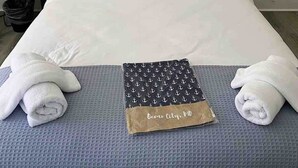 Ein Hotelzimmer mit Bett, Kissen, einem gerahmten Blumenbild, einem Nachttisch, einer Lampe und Handtüchern.