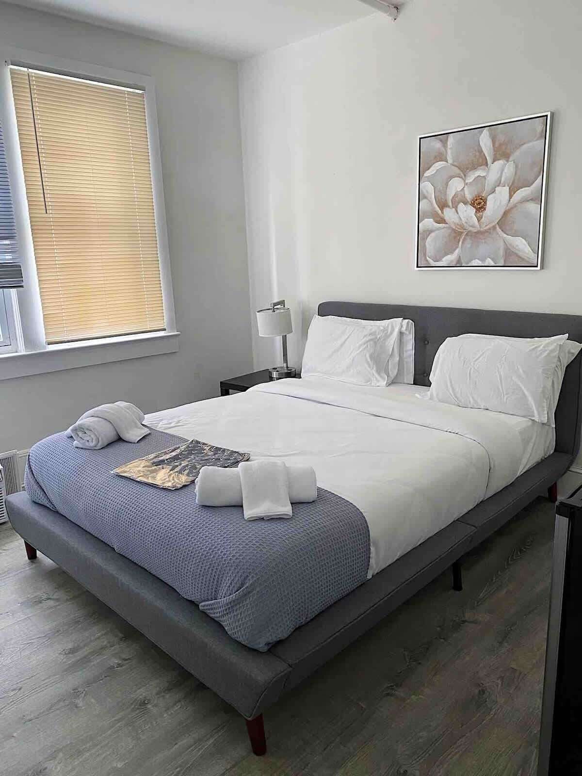 A neatly made bed with white linens, a grey headboard, and a blue textured blanket.