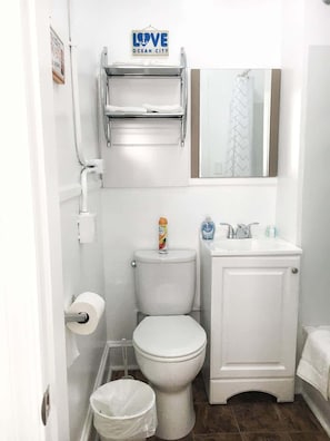 Un baño pequeño y blanco con inodoro, lavamanos, espejo y un cartel que dice 'LOVE OCEAN CITY' sobre el inodoro.