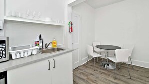 Et moderne køkken med mikrobølgeovn, vask og hvide skabe. Der er et spiseområde med et rundt bord og hvide stole.
