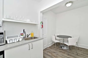 Una cocina moderna con microondas, pileta y armarios blancos. Hay un comedor con una mesa redonda y sillas blancas.