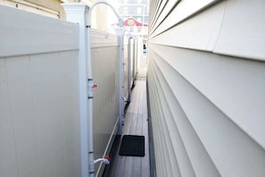 Un étroit passage entre deux bâtiments, avec une clôture blanche d’un côté et un bâtiment recouvert de bardage blanc de l’autre.