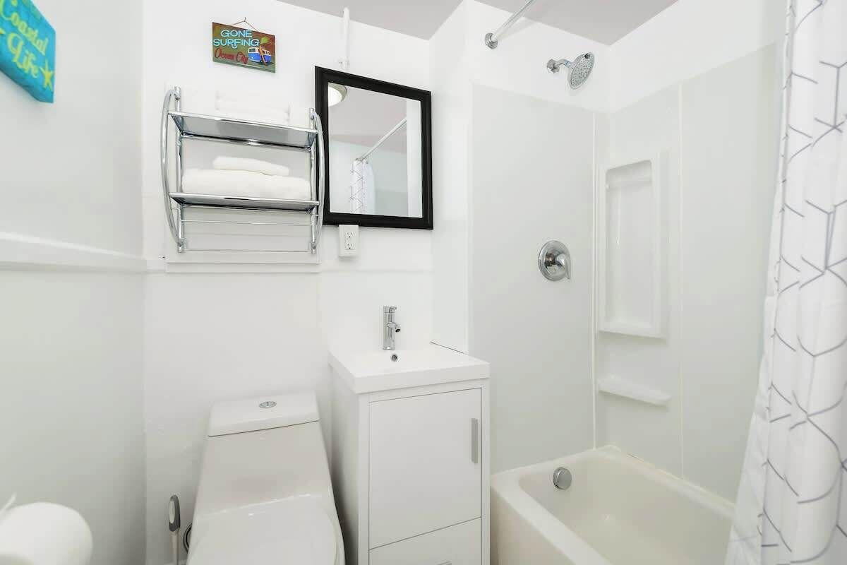 A bathroom with a toilet, sink, mirror, towel rack, and shower.