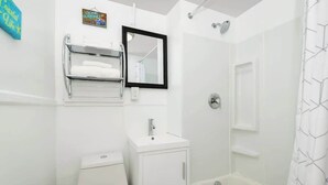 Baño con inodoro, lavamanos, espejo, toallero y ducha.