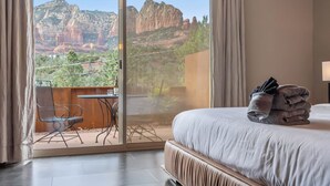 A hotel room with a bed, a table with chairs, and a view of red rock formations.