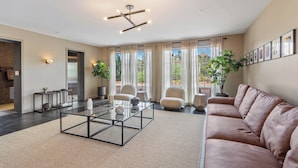 A modern living room with a sectional sofa, a glass coffee table, and a large window with curtains.