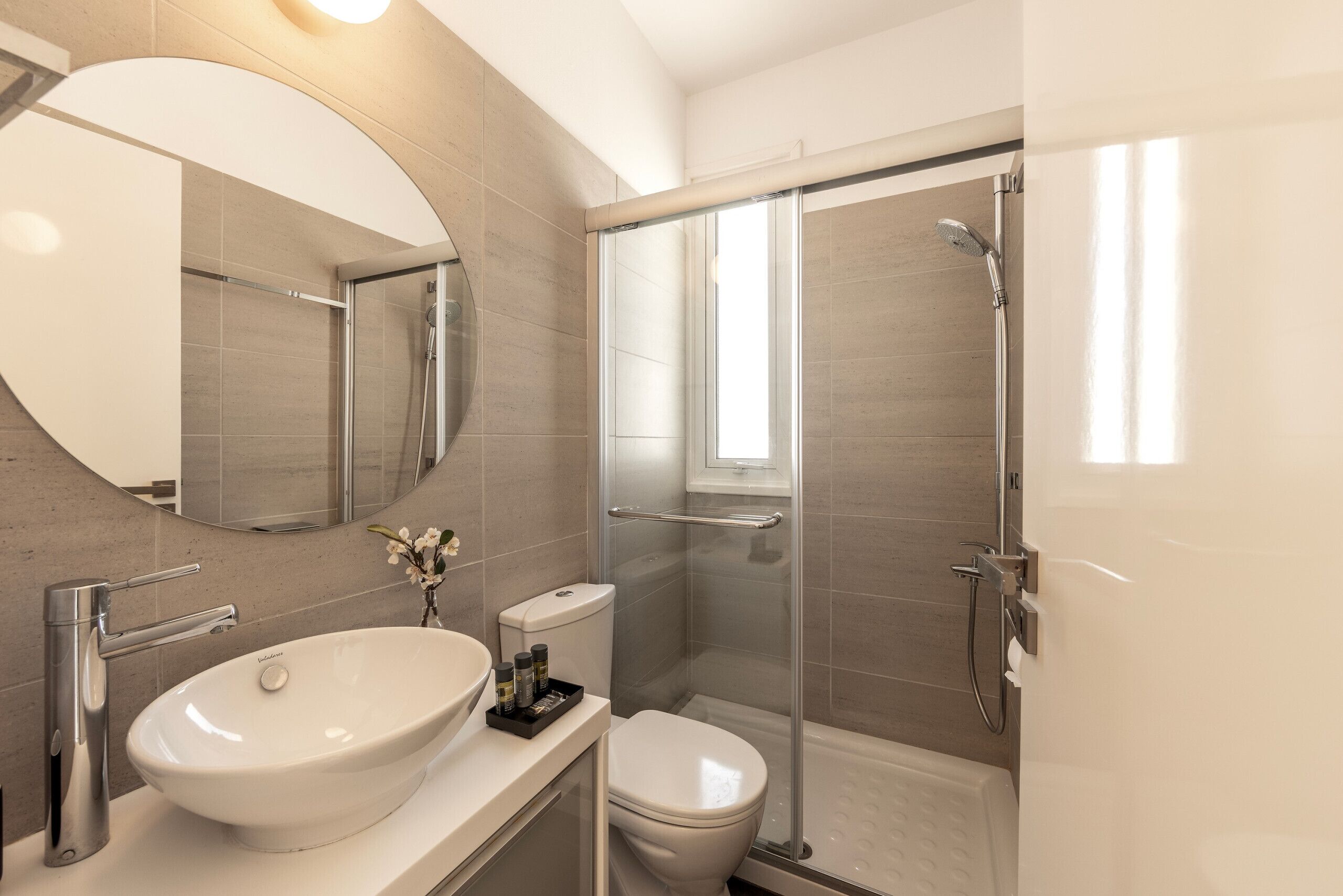 A modern bathroom with a large oval sink, a toilet, and a glass-enclosed shower area.