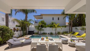 Un espace aménagé au bord de la piscine, avec des chaises longues, une table où sont servis des boissons et une vue sur un bâtiment en arrière-plan.