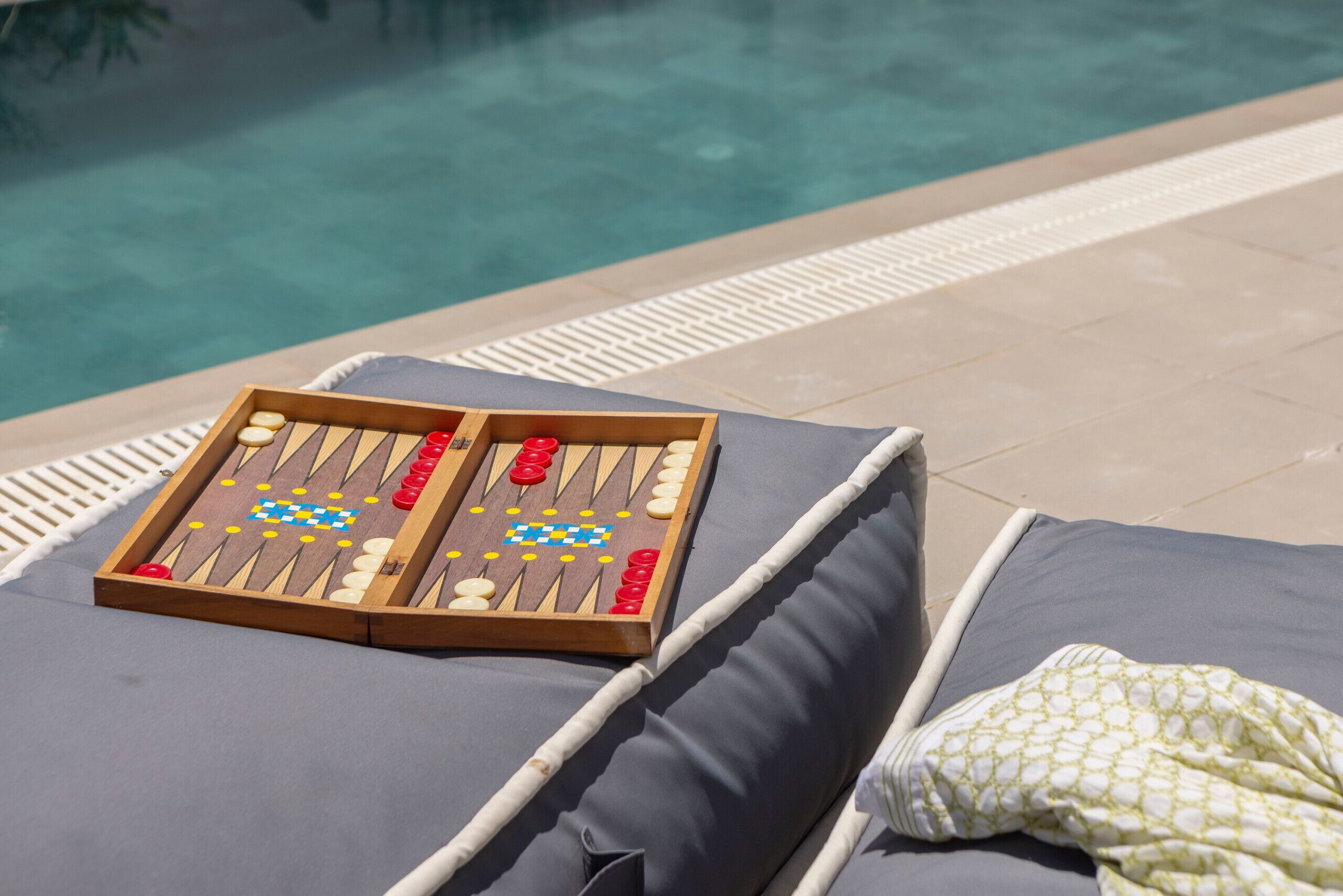 A poolside lounge area with a backgammon set on a cushioned chair.