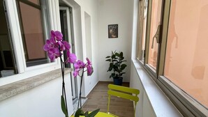 A narrow balcony with a yellow table and two chairs, a potted plant, and a window with a view.