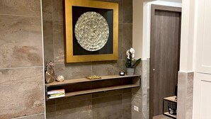A modern bathroom with a herringbone wood floor, a built-in shelf with decorative items, and a large circular mirror framed in gold.