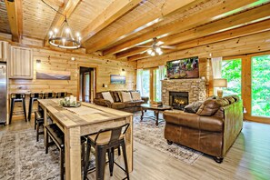 L’intérieur d’une cabane en rondins comprend un coin repas, un salon, une cheminée et de grandes fenêtres.