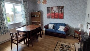 A living room with a wooden dining table, blue sofa, and a radiator. - Abbeyfeale Home-sleeps 6 -private Garden (Abbeyfeale)