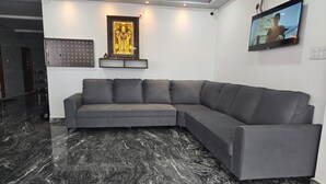 A modern living room with a grey sectional sofa, a framed religious statue, a wall-mounted TV, and a decorative light fixture. - Om Sri Vigneshwara Palani Grand Hotel (Hyderabad)