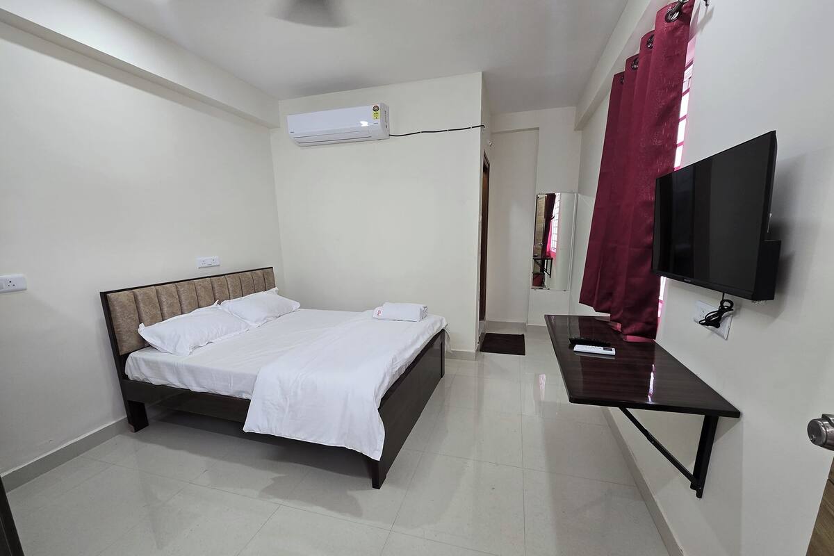 A hotel room with a bed, a desk, a TV, and an air conditioning unit.
