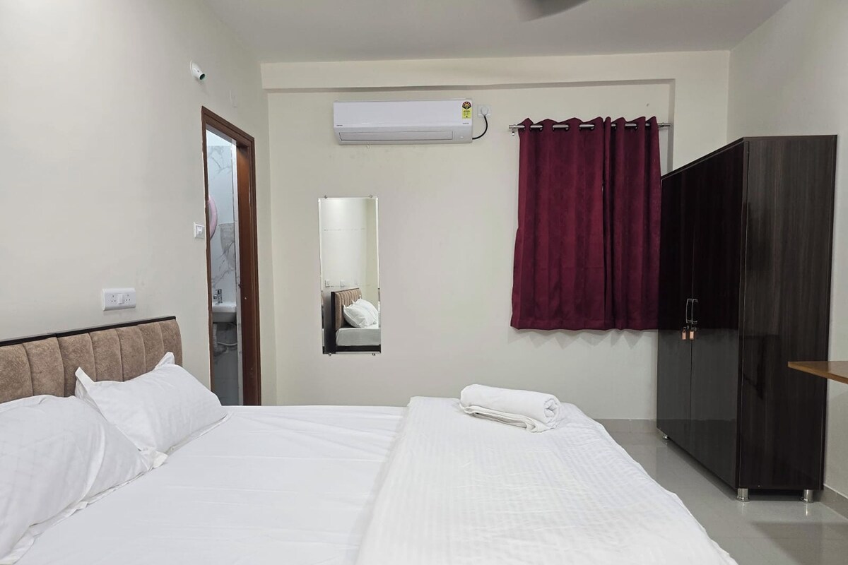 A hotel room with a bed, a wardrobe, a mirror, and an air conditioning unit.