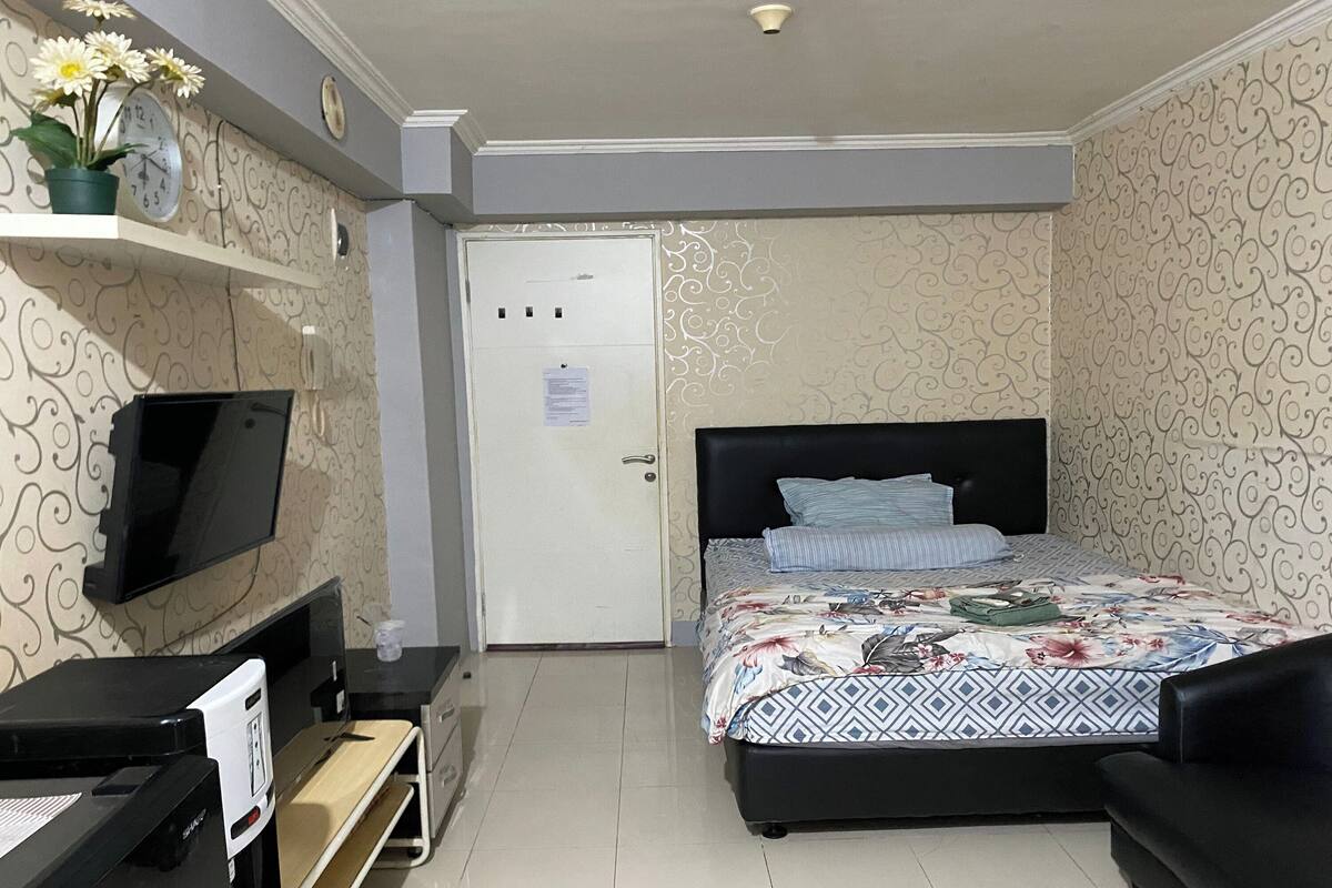 A bedroom with a bed, a TV, a desk, and a door.
