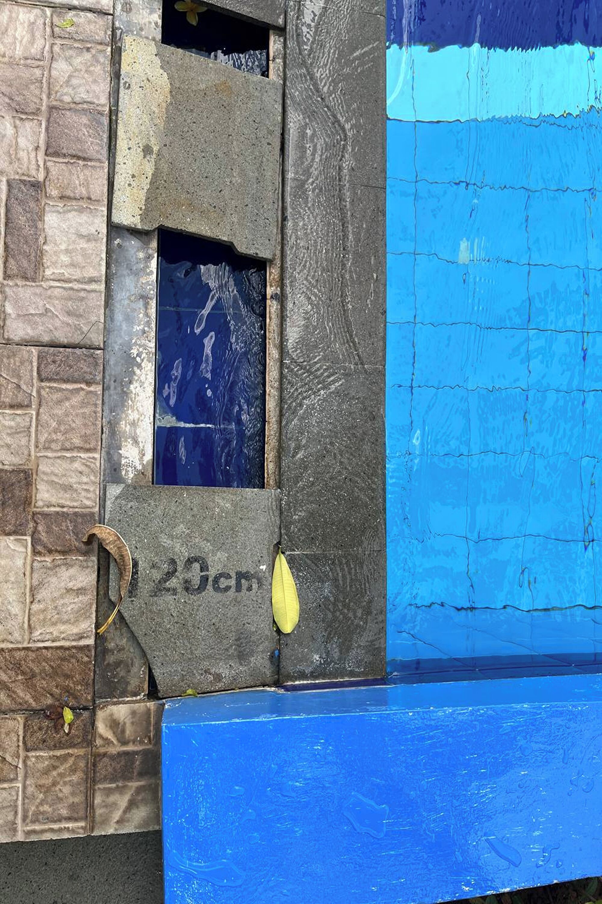 A building facade with a stone wall, a blue painted section, and a window with a number plaque.