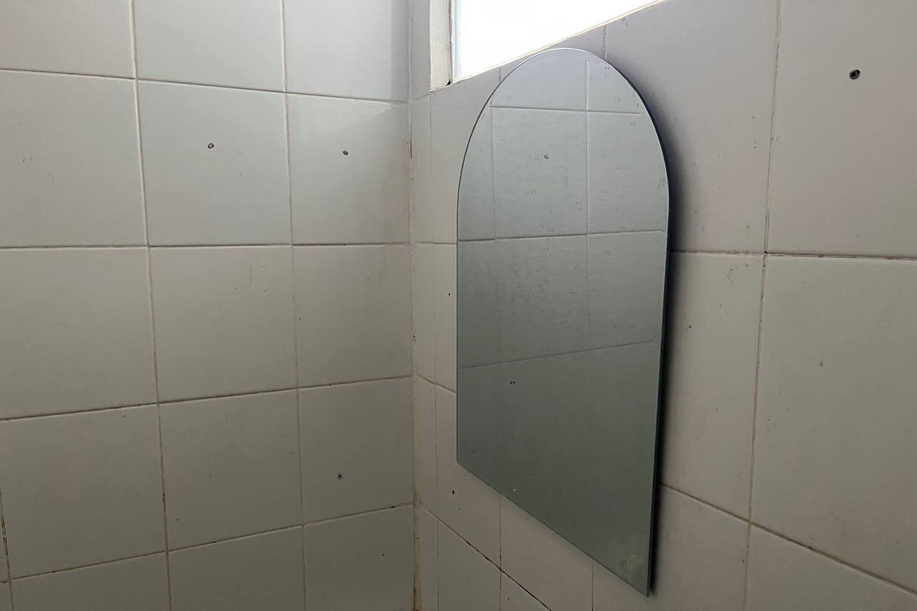 A tiled bathroom with a large, curved mirror on the wall.