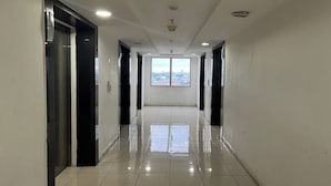 A clean, modern hallway with a shiny tiled floor, glass doors, and a large window at the end offering a city view.