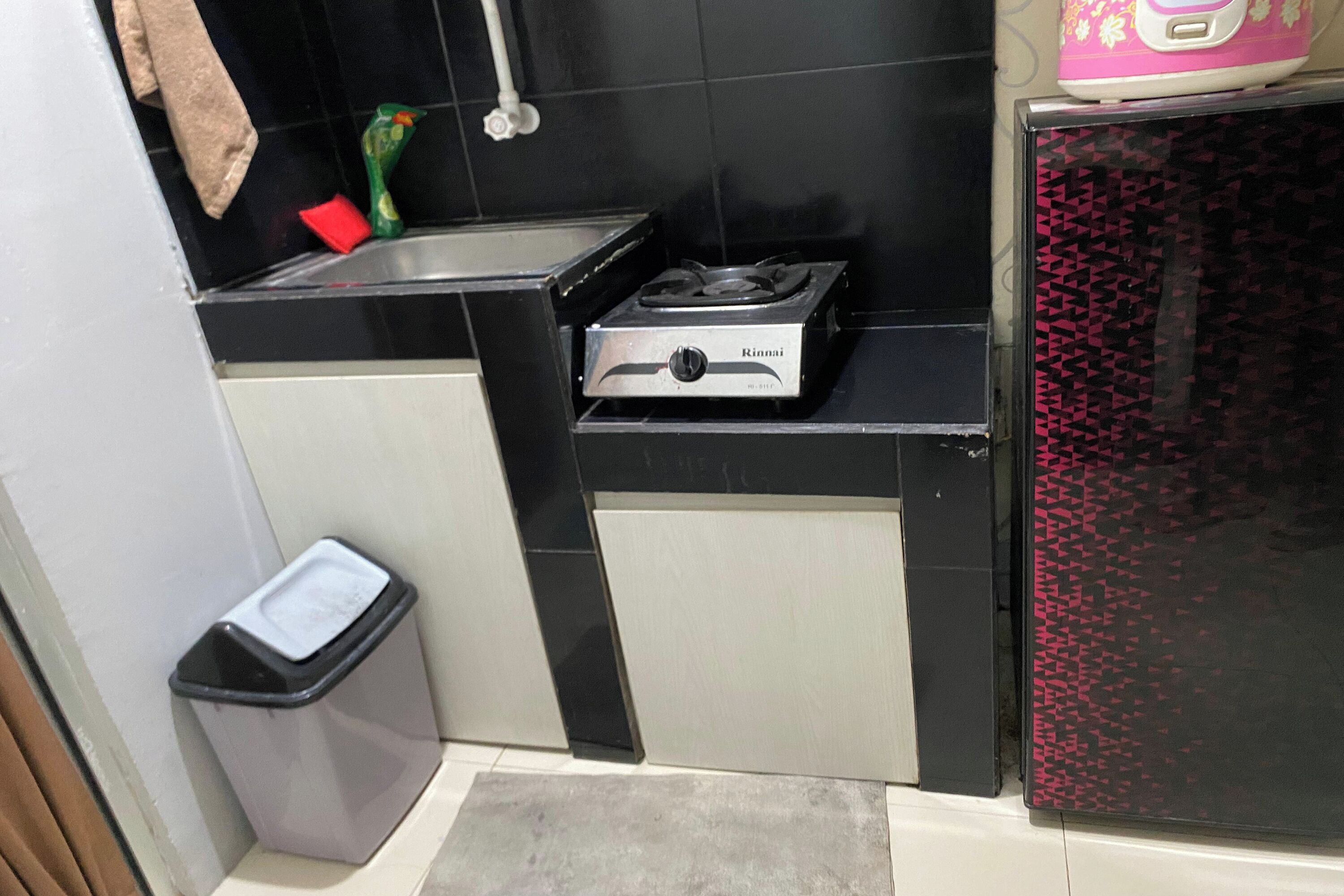 A compact kitchen with a gas stove, a trash bin, and a refrigerator.