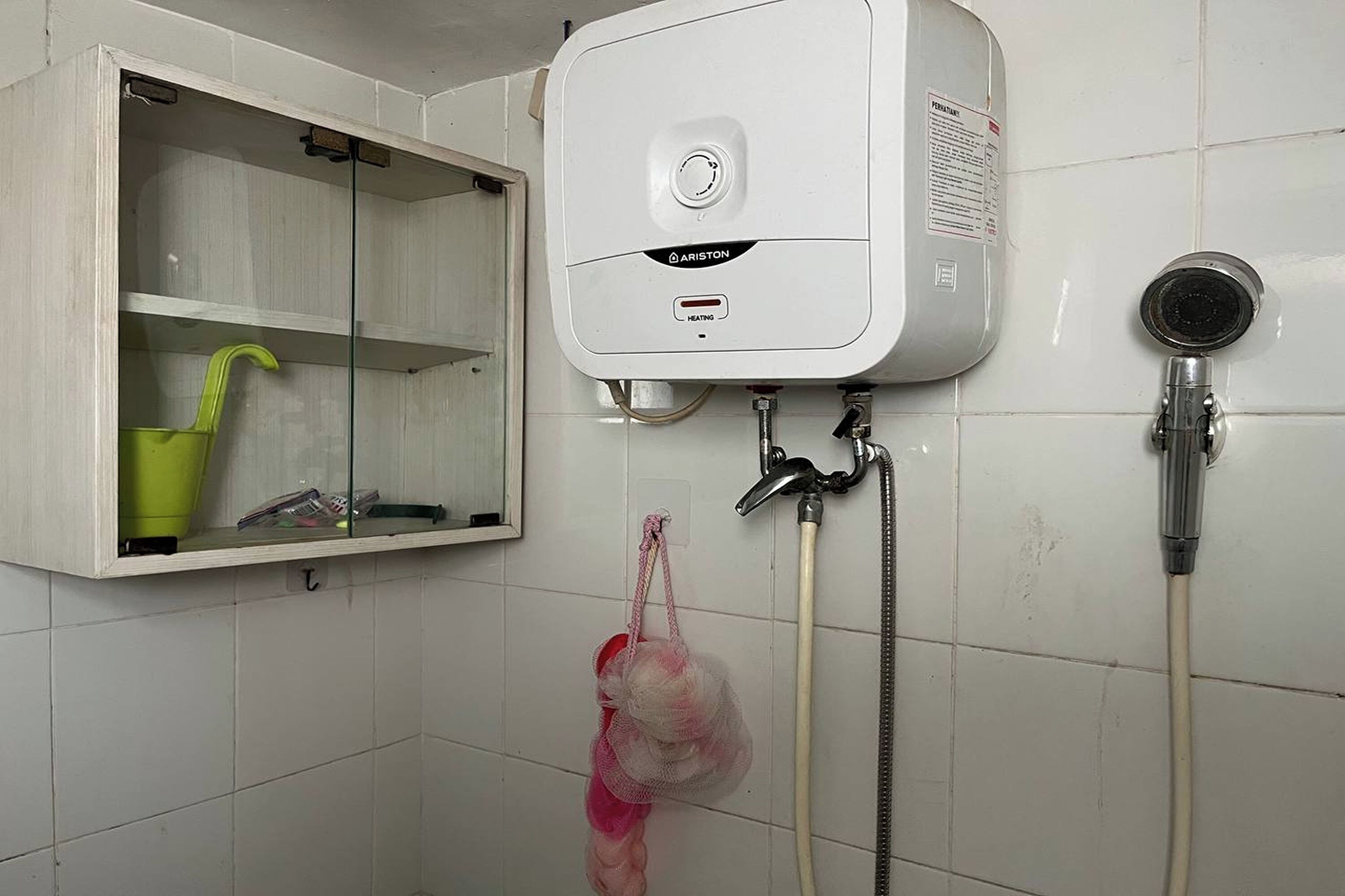 Un baño con un calentador blanco, un cabezal de ducha y un armario con un recipiente verde.