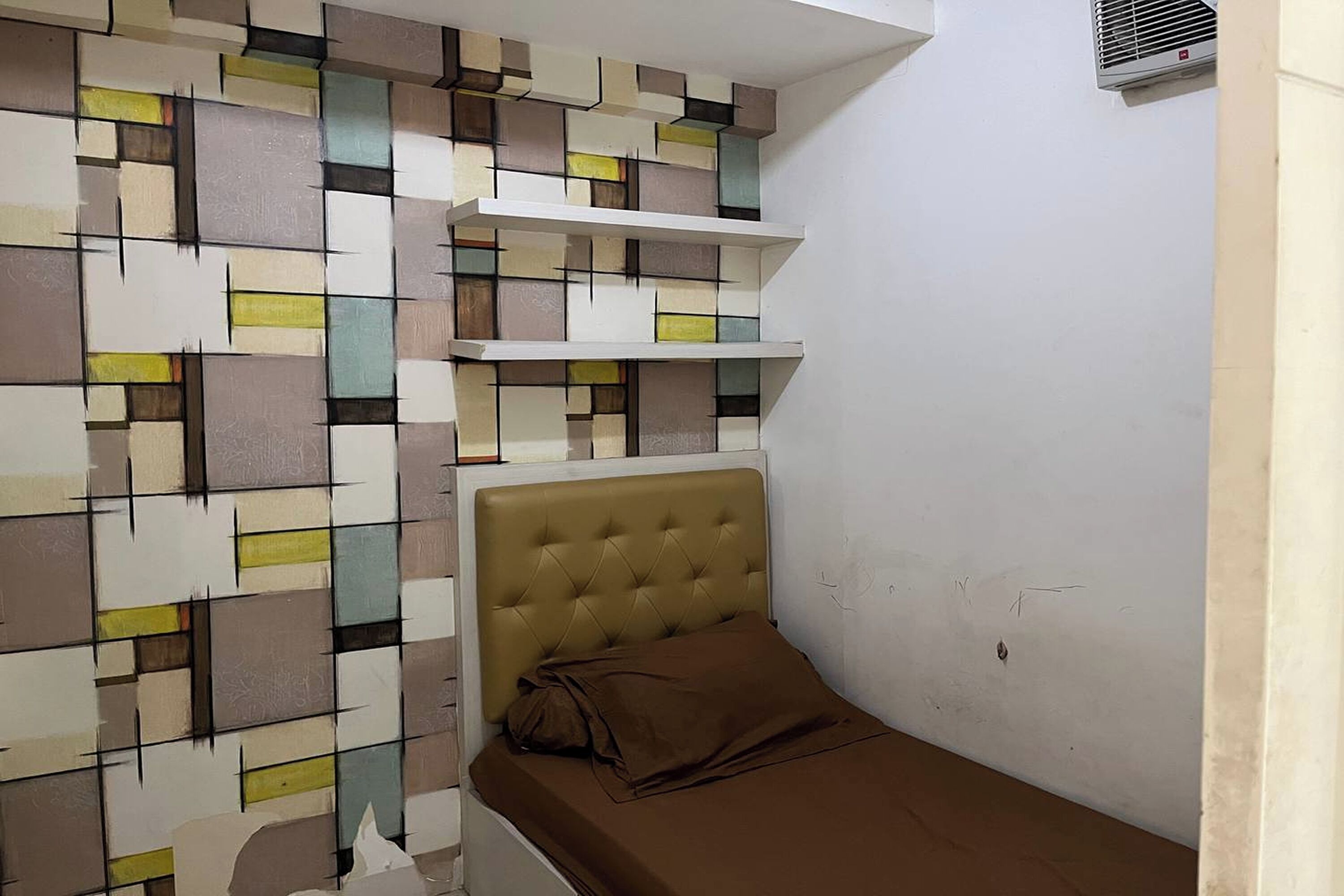 A bedroom with a bed, a headboard, and a wall with a geometric pattern.