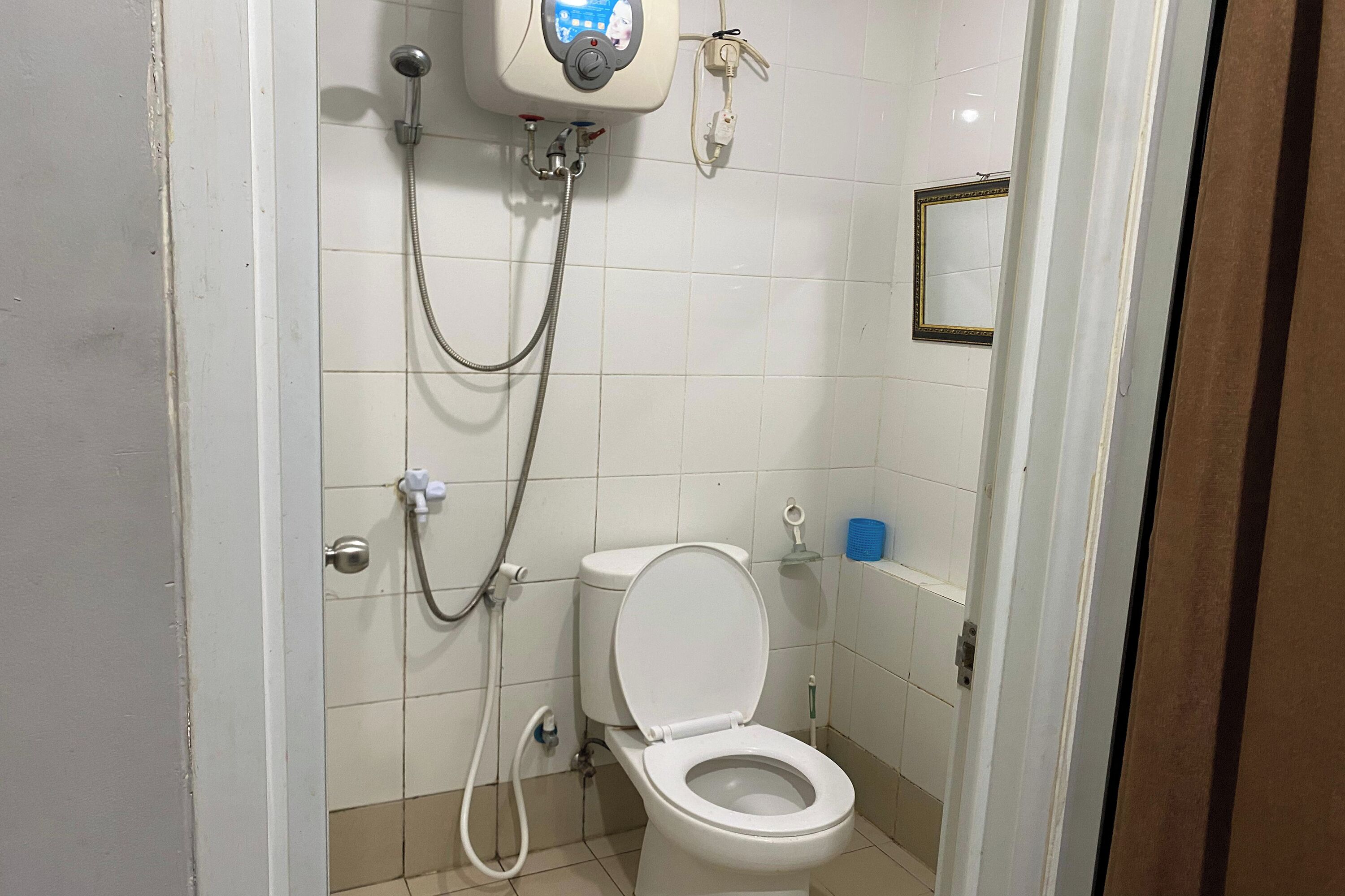 A bathroom with a toilet, a shower unit, and a mirror on the wall.