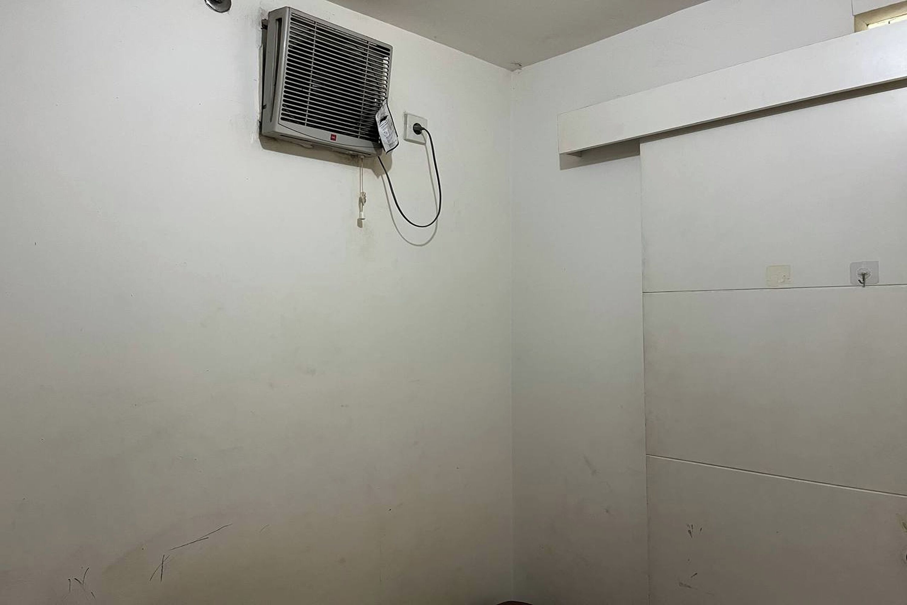 A bathroom with a wall-mounted air conditioner, a towel rack, and a plain tiled wall.
