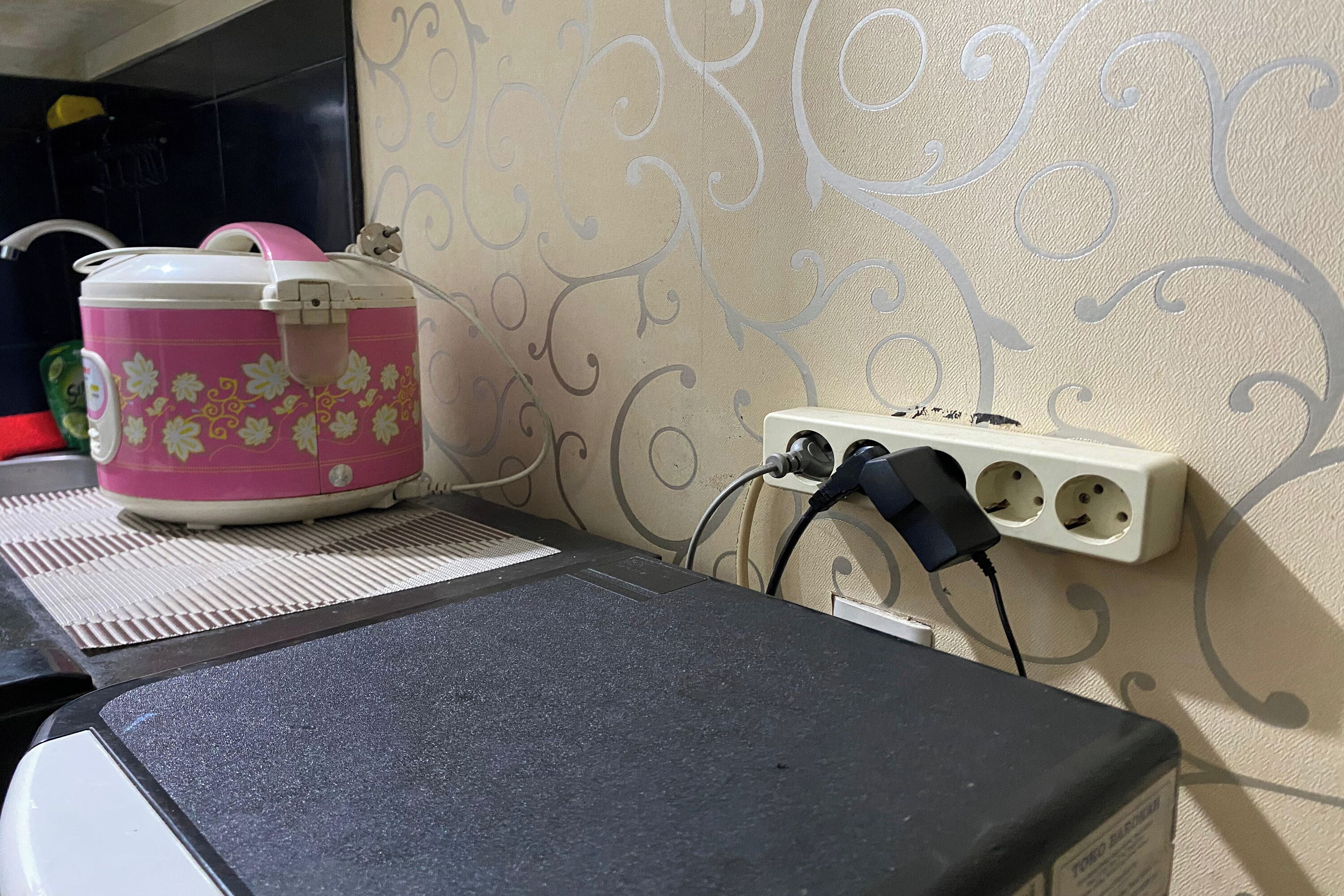 Eine Küchenarbeitsplatte mit einem rosa Gerät, einer Mehrfachsteckdose und einer Wand mit dekorativen Mustern.