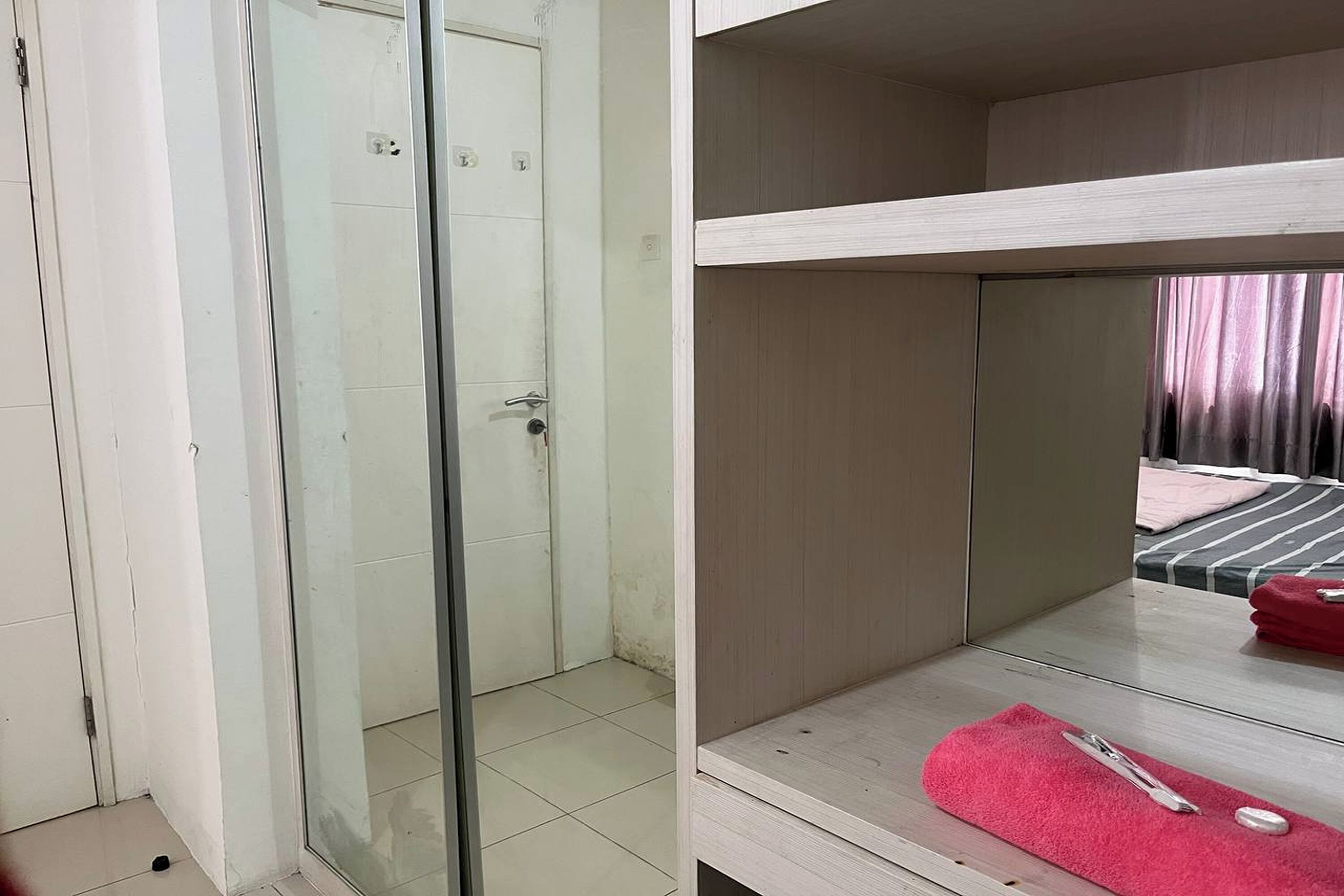 Una habitación con mampara de vidrio, una cama con toalla roja y un estante de madera.