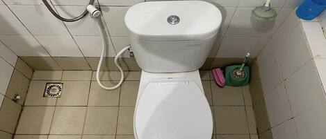 Et hvidt toilet med bidét, en lille skraldespand og en toiletbørste.