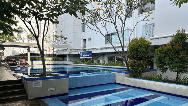 A swimming pool with blue tiles, surrounded by trees and a building with windows.