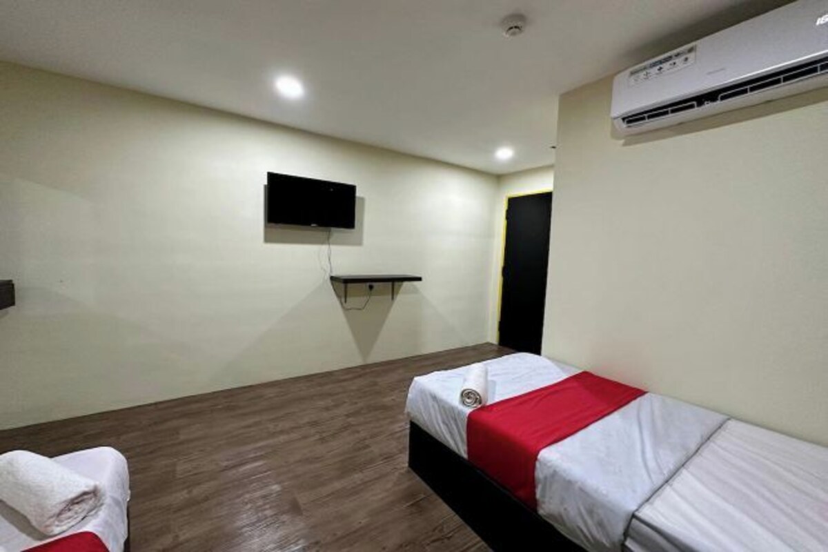 A hotel room with two beds, a mounted TV, and an air conditioning unit.