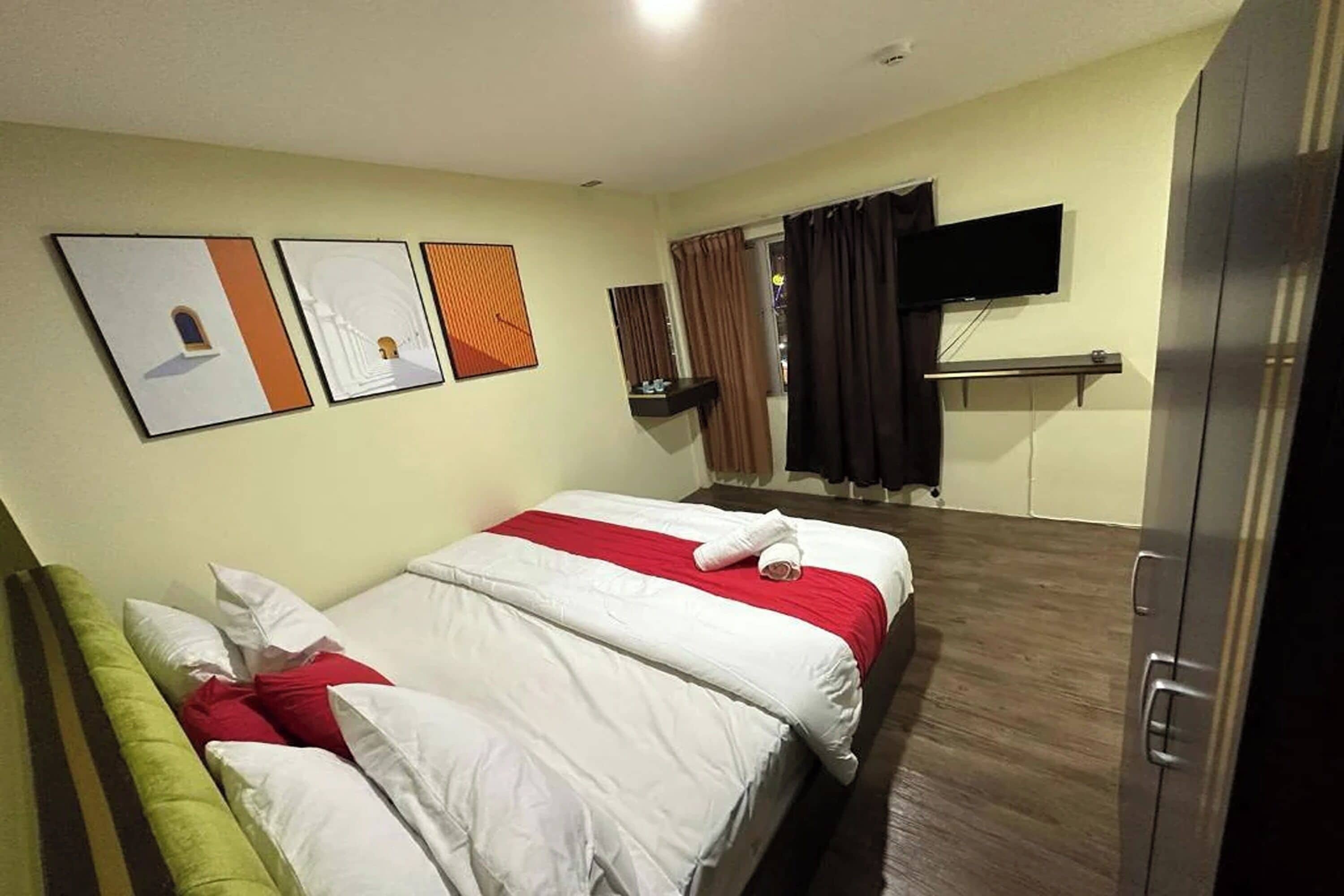 A hotel room with a bed, a flat-screen TV mounted on the wall, and artwork on the wall.