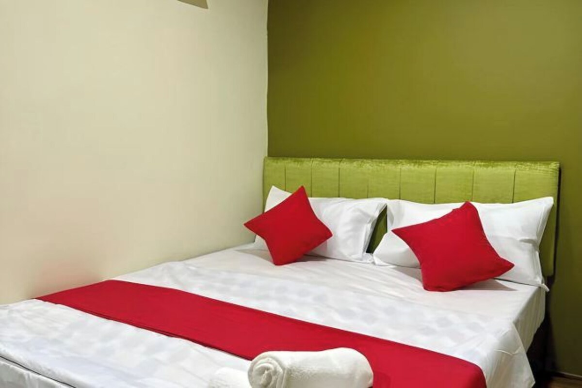 A neatly made bed with white and red bedding, a green headboard, and a red accent pillow.