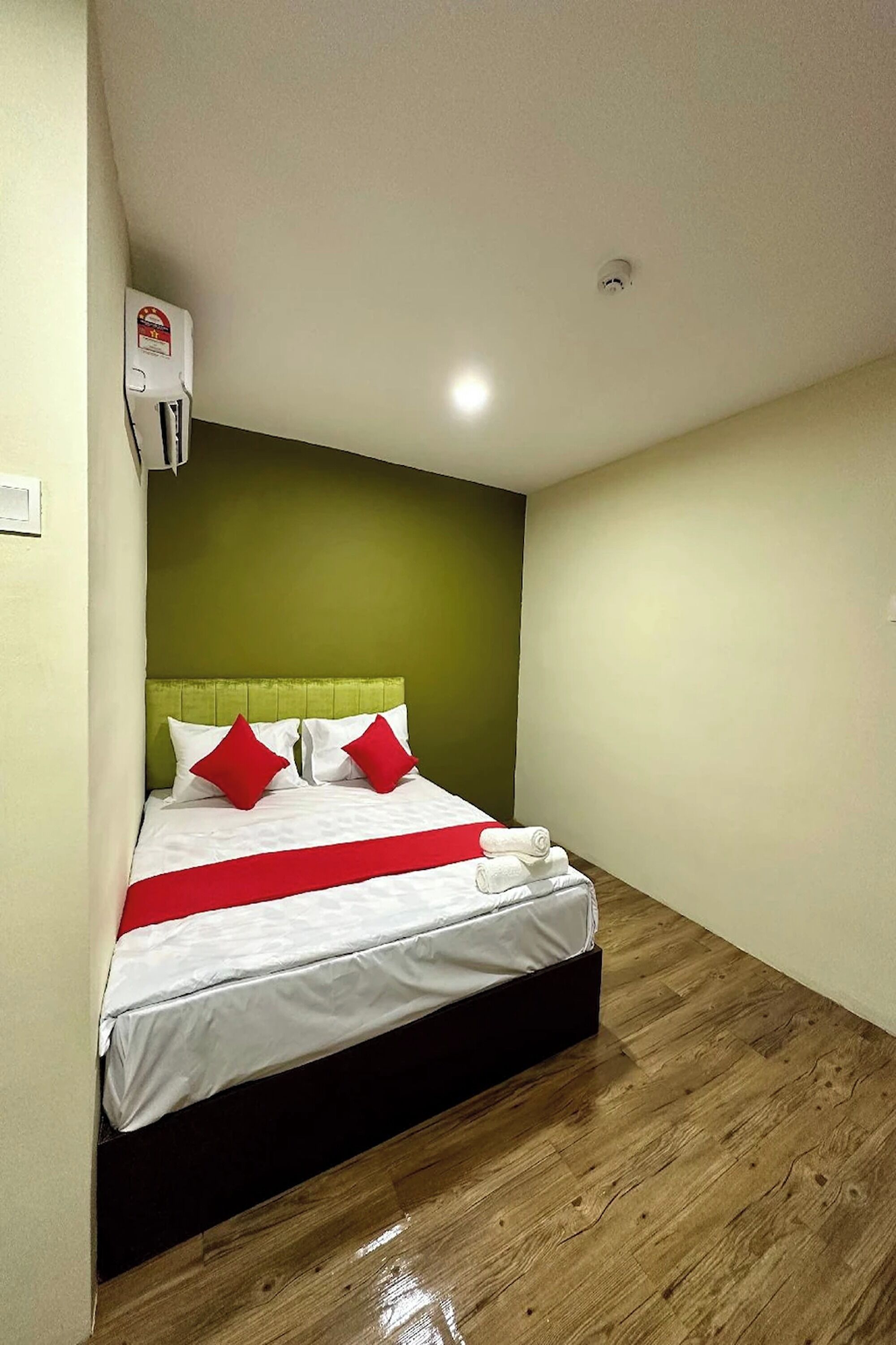 A neatly made bed with white bedding and red accents, a green accent wall, and a wooden floor.