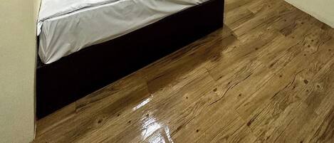 A neatly made bed with white bedding and red accents, a green accent wall, and a wooden floor.