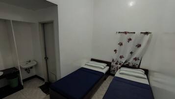 Una habitación pequeña y limpia con dos camas individuales, un lavamanos y ducha.