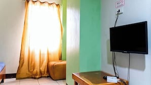 A room with a television mounted on the wall, a wooden table, a sofa, and a window with curtains. - Green Ridge Apartelle (Malaybalay City)