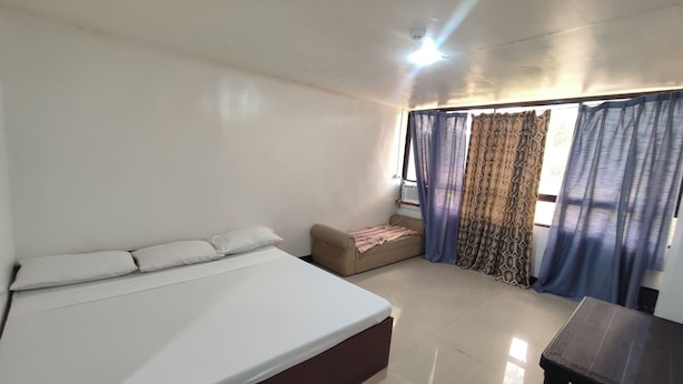 A room with a bed, a small sofa, a table, and curtains. - Green Ridge Apartelle (Malaybalay City)