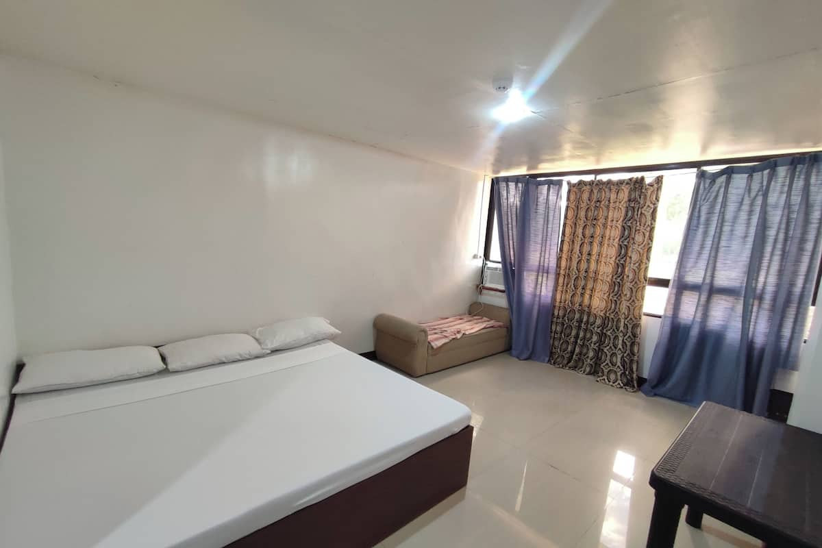 Una habitación con cama, un sofá pequeño, una mesa y cortinas.