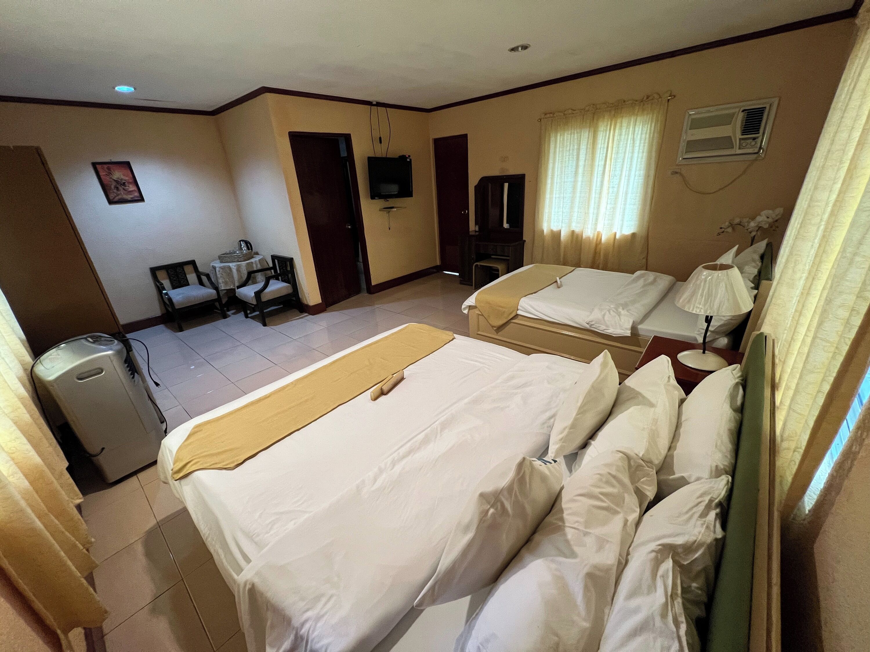 A hotel room with two beds, a desk, a chair, a television, and an air conditioning unit.
