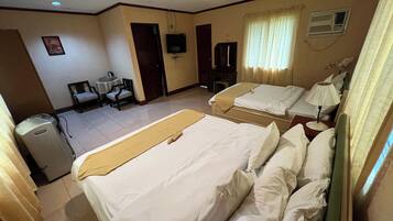 A hotel room with two beds, a desk, a chair, a television, and an air conditioning unit.