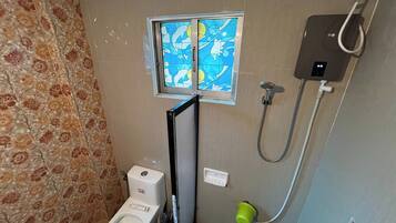 A bathroom with a toilet, a shower, and a window with a floral pattern.